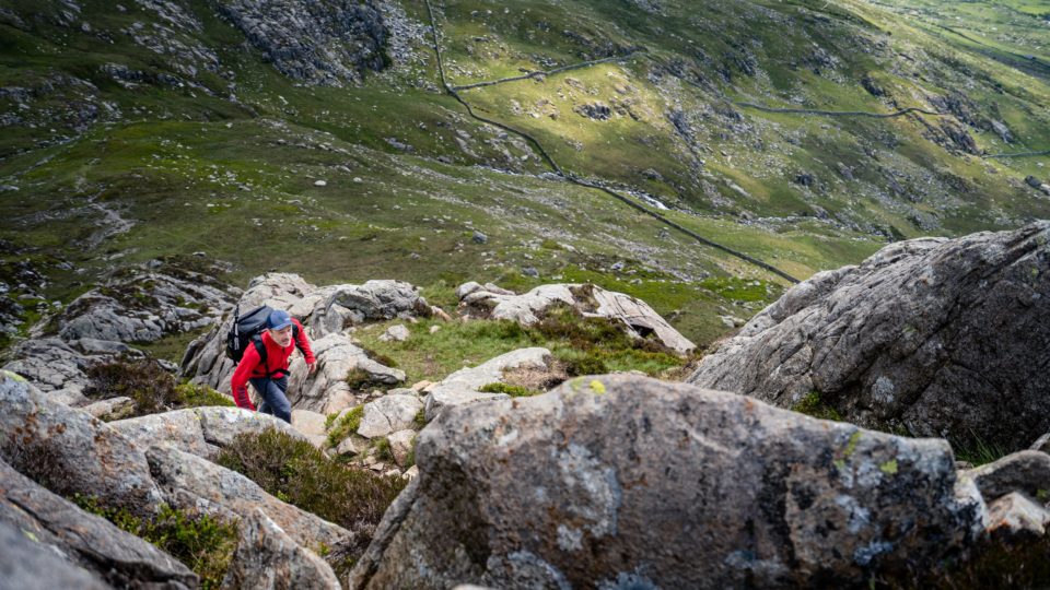 man hiking up rocks in green hills