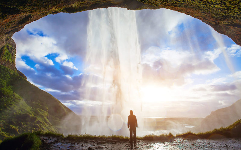 man stands under waterfall in Iceland