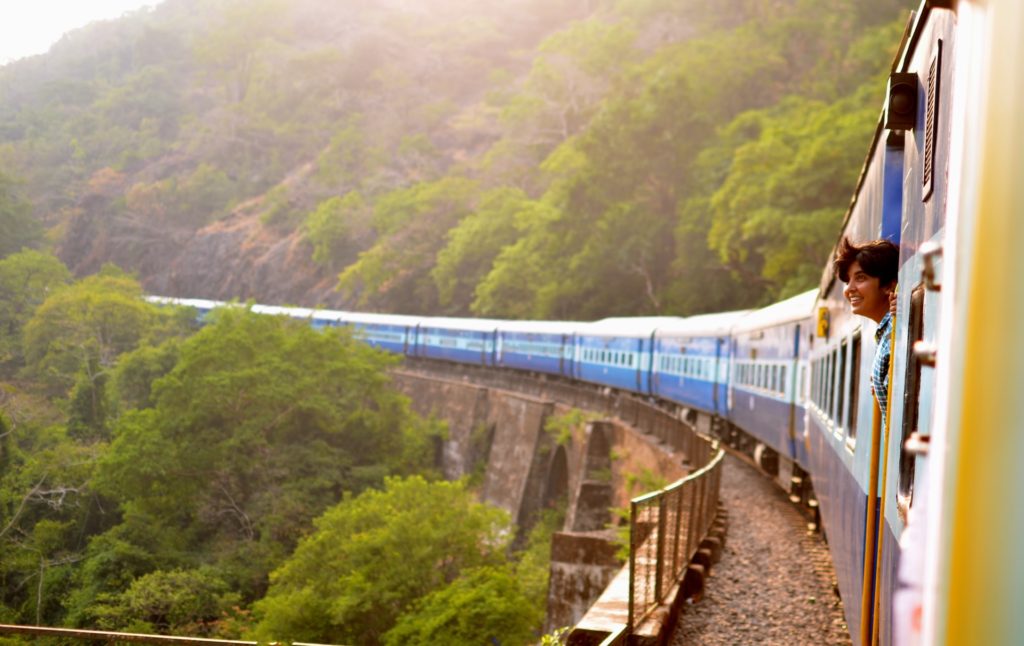 person smiling on moving train in green trees