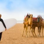 female surfer and camels on beach