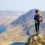 male hiker stands to admire mountain valley