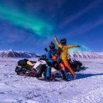 tourists on snowmobile under northern lights